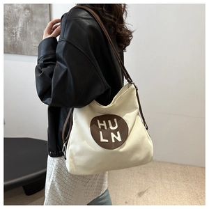 Detail view of canvas tote bag with leather HULN patch and dark brown shoulder straps