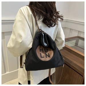 Model wearing a black canvas tote bag with brown leather strap and HU LN print