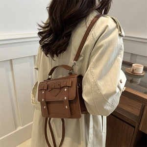 Brown vintage college messenger bag with heart bow detail on a trench coat model