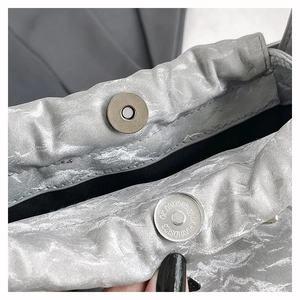 Vue macro du fermoir magnétique sur un sac à bandoulière argenté avec détails plissés