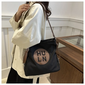 Detail of black canvas tote featuring HULN leather patch and adjustable brown strap