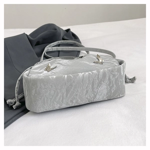 Détail d'un sac à main plissé argenté métallisé avec charmes papillon et cordons de serrage