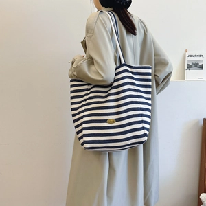 Large striped canvas tote bag with handmade patch shown on a model in trench coat