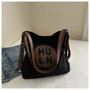 Detail of adjustable brown faux leather straps and metal buckles on black canvas tote bag