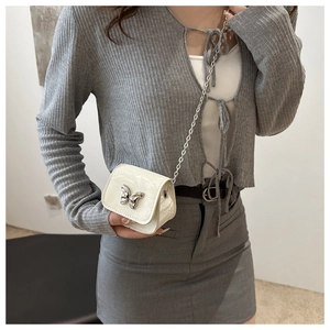 Close-up of a white patent leather saddle bag with silver butterfly and chain strap