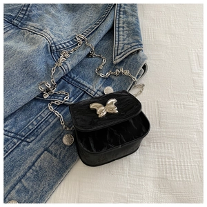 Detail of black pleated crossbody bag featuring a silver butterfly clasp and chain strap