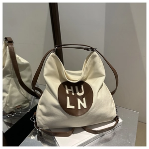 Detail of canvas tote bag showing contrast leather strap and circular logo patch on white fabric
