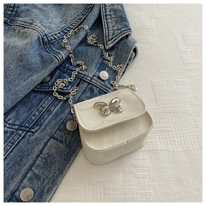 Close-up of a white textured crossbody bag with a silver butterfly clasp on denim fabric