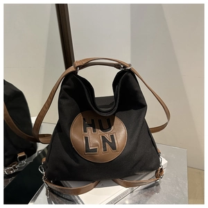 Detail of black canvas tote bag showing brown leather handles and HULN letter patch