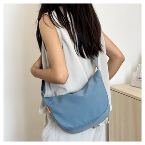 Blue nylon dumpling bag with orange tag detail and adjustable strap on model back
