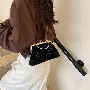 Elegant black velvet shell bag with white dots and gold chain strap worn by a model