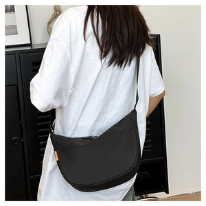 Detail of a black nylon crescent crossbody bag with an orange tag worn by a model