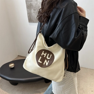 Large beige canvas tote bag with brown leather straps worn by a model in casual style