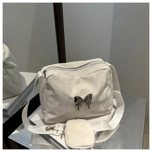 Detail of cream crossbody bag featuring a metallic butterfly logo and wide strap