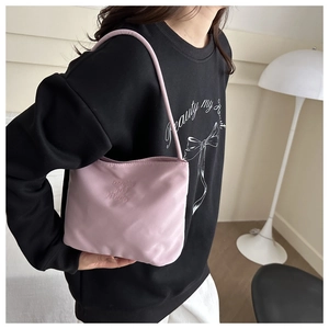 Detail of soft pink bucket bag with 3D embossed text worn on a woman's shoulder