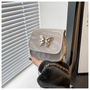 Close-up of light gray crossbody saddle bag with silver butterfly charm and chain strap