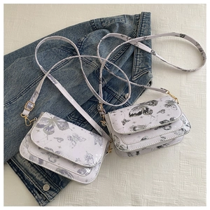 Detail of white butterfly print crossbody bag with gold hardware on denim jacket