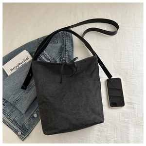 Close-up of a dark grey denim bucket bag featuring a black bow detail and leather strap