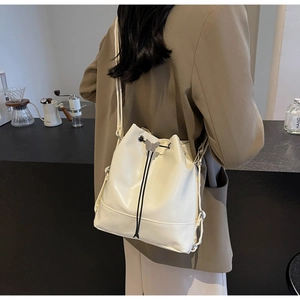 Detail view of cream bucket bag with drawstring closure and metal butterfly ornament