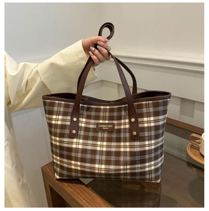 Detail of classic plaid tote bag with brown faux leather handles and metal rivets