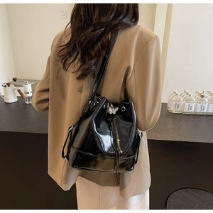Detail of a black glossy bucket bag with a silver butterfly buckle worn on a shoulder