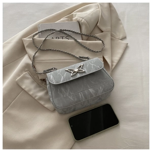Detail of silver butterfly clasp and marble texture on a grey crossbody chain bag