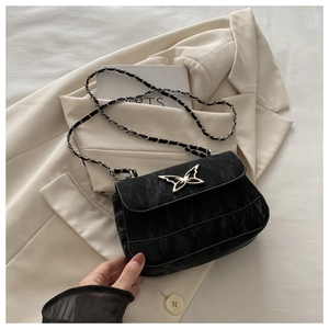 Close-up of black textured crossbody bag featuring metal butterfly clasp and chain strap