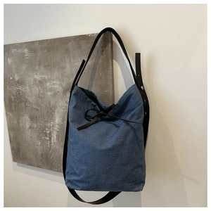 Detail of blue denim bucket bag featuring black leather drawstring bow and textured fabric