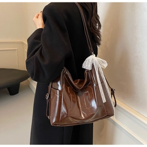 Detail of dark brown glossy leather tote bag with number ten and white lace bow decoration