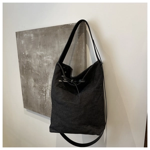 Detail of a black minimalist canvas tote bag featuring a leather strap and bow decoration