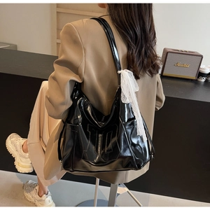 Detail of large black glossy tote bag with stylish white lace scarf accessory on strap
