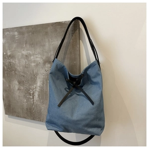 Close-up of blue denim bucket bag featuring a black decorative bow and leather strap