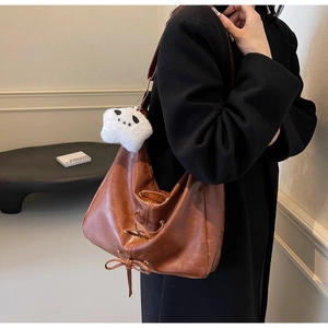 Brown leather tote with lace-up detail and plush panda charm worn by a model