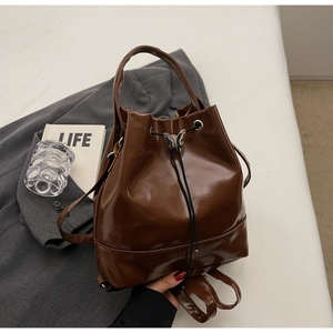 Macro detail of deep brown glossy leather bucket bag with silver butterfly charm