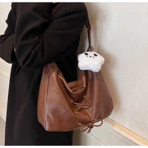 Detail of a brown PU leather hobo bag with lace-up design and a cute plush bear pendant
