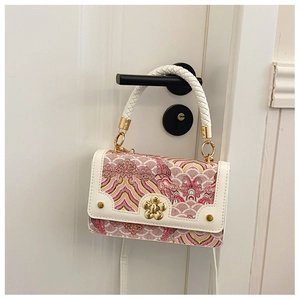Detailed shot of tricolor woven crossbody bag with gold floral lock on white door handle