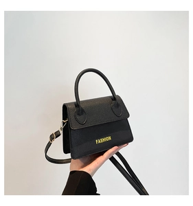 Detail of black litchi grain handbag with yellow FASHION text and top handle