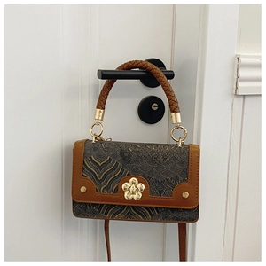 Detail of a chic shoulder bag with gold wave patterns and flower-shaped metal clasp