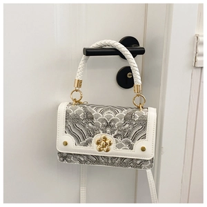 Detailed shot of white crossbody bag with wave pattern embroidery and gold floral buckle