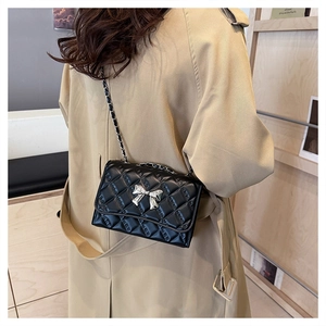 Detail of black quilted leather crossbody bag featuring a silver metal bow accent