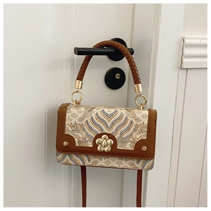 Close-up of wavy embroidery patterns, woven handle and floral metal buckle on a small bag