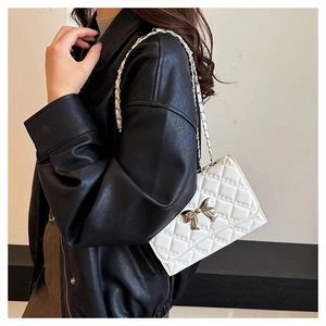 Close-up of white quilted leather bag featuring a silver bow lock and chain strap