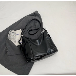Detailed view of black polished leather large hobo bag with wide shoulder strap on a grey blazer