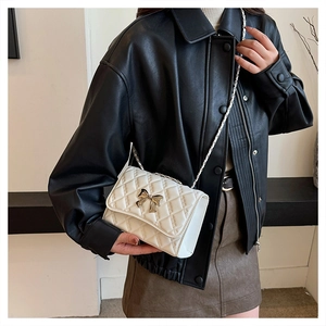 Close-up of white quilted crossbody bag featuring a golden bow and chain strap