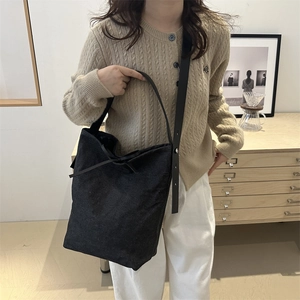 Minimalist black canvas tote bag with bow detail and leather shoulder strap in a cozy room