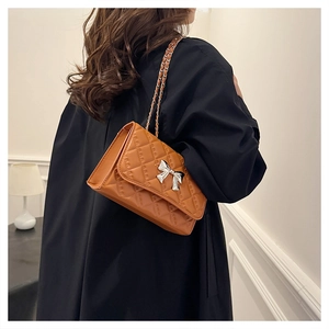 Detail of a brown quilted leather crossbody bag with silver bow buckle on black coat