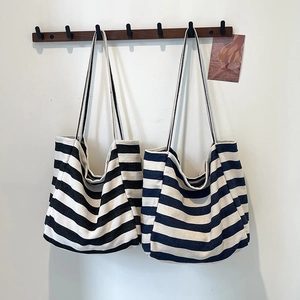 Minimalist striped canvas tote bags in black and blue shown hanging on a wooden wall hook