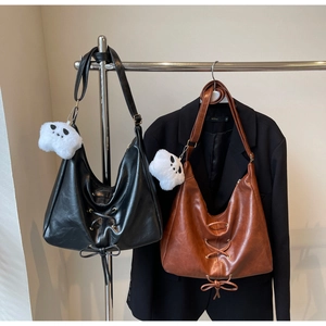 Detail of black and brown leather hobo bags with lace-up accents and plush charms