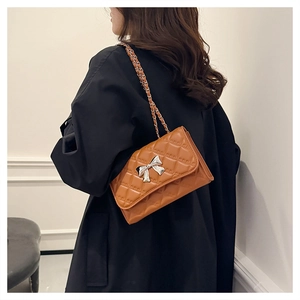 Brown quilted crossbody bag with silver bow buckle worn on a black coat back view