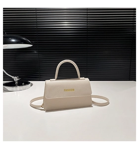 Detail of lychee textured cream crossbody bag with gold fashion lettering and thin strap